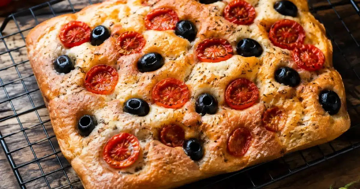 Focaccia dorata con pomodorini rossi e olive nere su griglia
