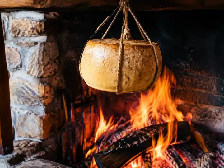 Formaggio affumicato appeso sopra fuoco vivo nel camino rustico