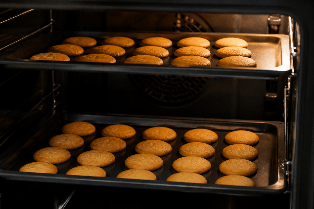 Teglie di biscotti dorati uniformemente nel forno ventilato.
