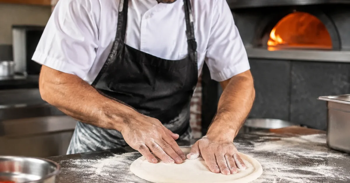 Pizzaiolo stende l'impasto con le mani sul banco