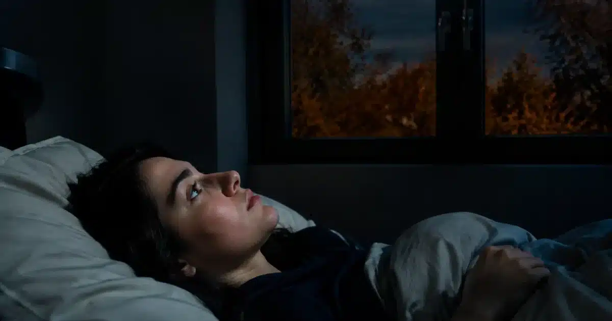 Persona sdraiata nel letto al buio con finestra chiusa durante sera autunnale